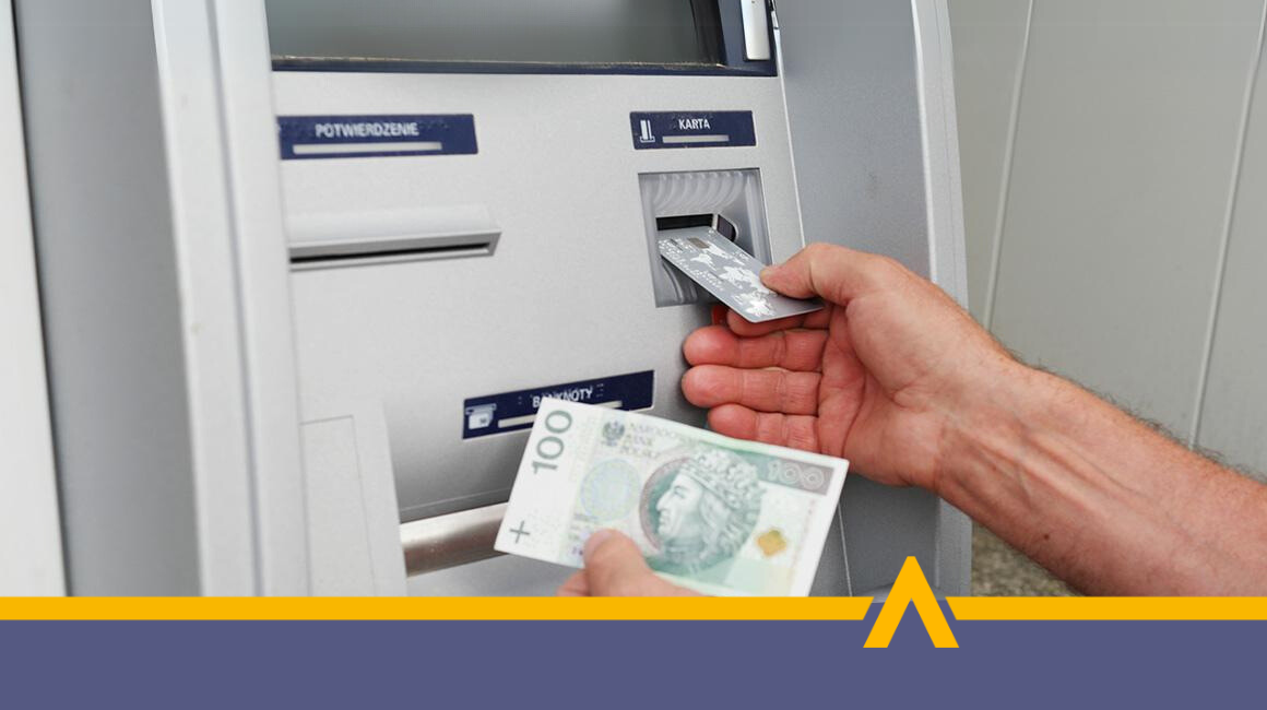 Osoba wypłacająca gotówkę z bankomatu – karta płatnicza i banknot 100 złotych