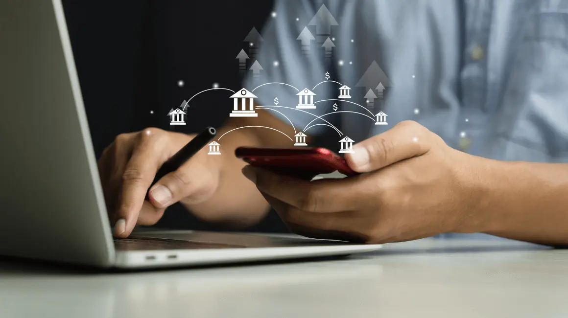 Mężczyzna wykonujący przelewy między bankami za pomocą telefonu i laptopa